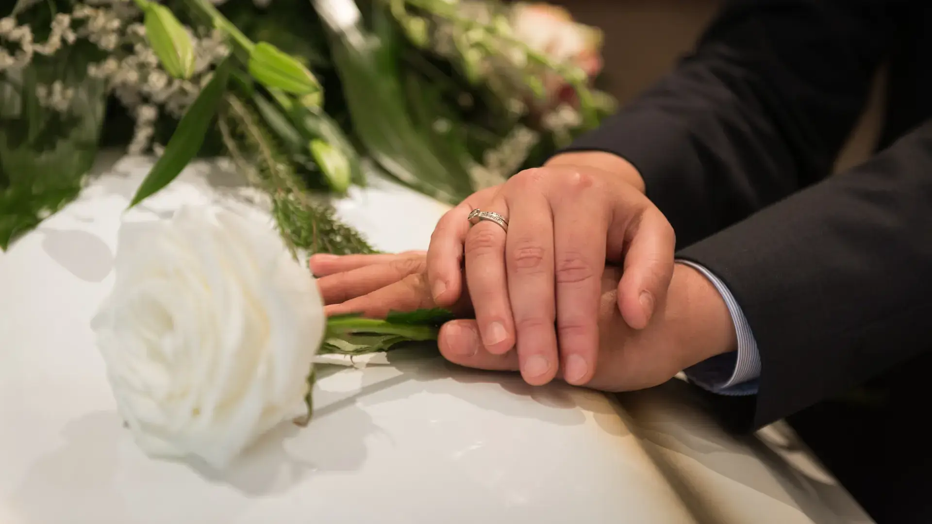 Hands resting gently on a casket adorned with white flowers at Kane Fetterly Funeral Home in Montreal