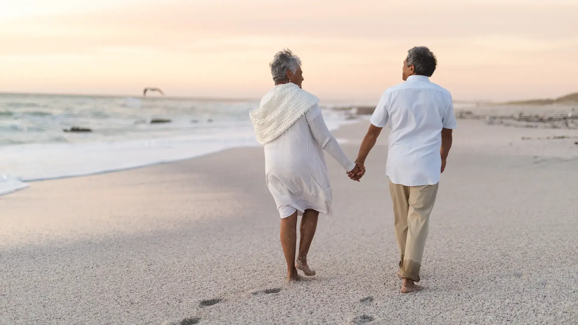 Senior couple walking hand in hand along the beach, symbolizing peace, reflection, and togetherness